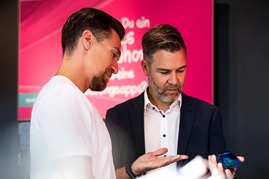 Zwei Männer betrachten Smartphone, Beratung zu App und digitalem Service am Stand